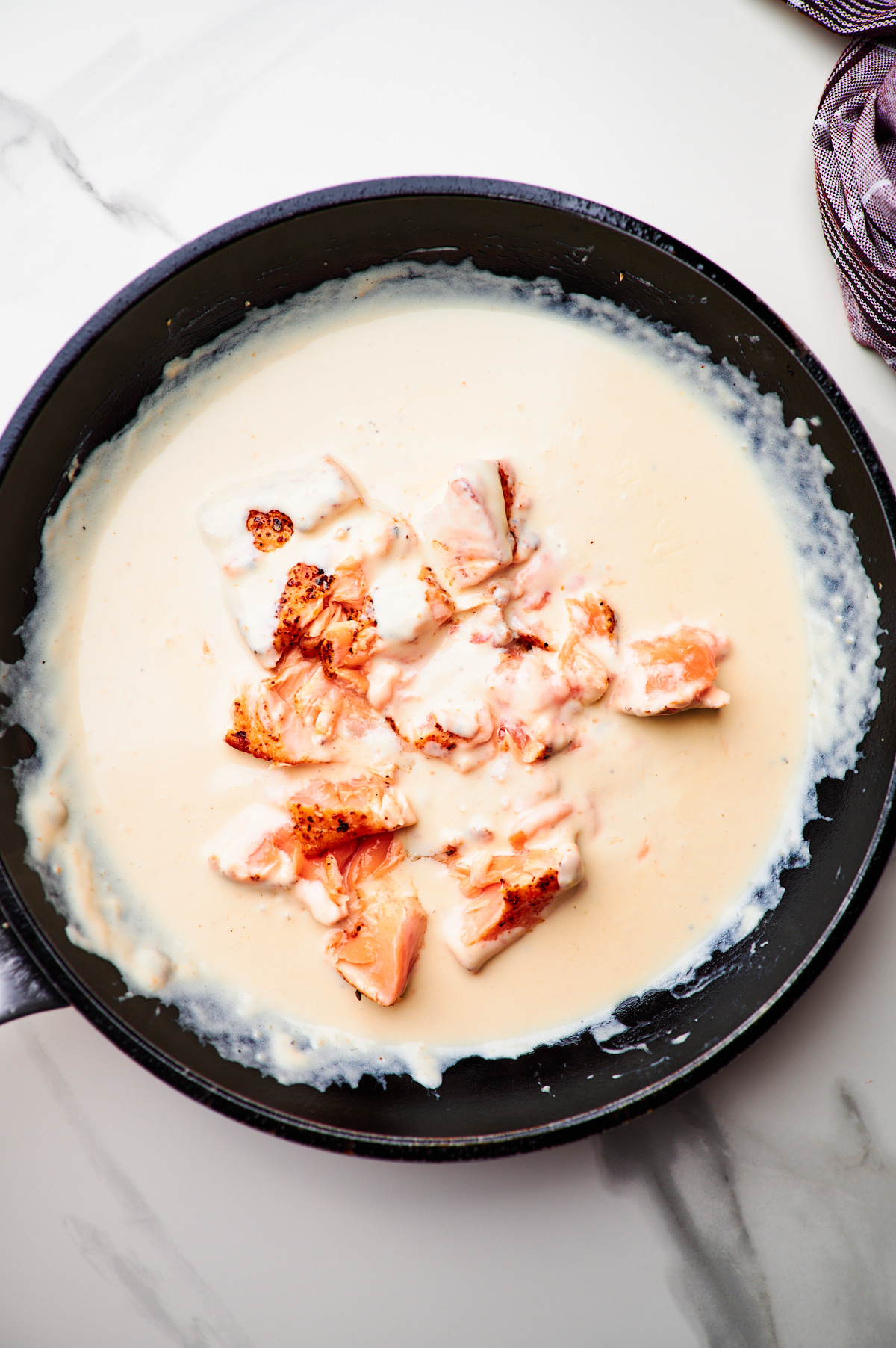 adding salmon back into the sauce for creamy garlic salmon pasta and then mixing in spaghetti with tongs