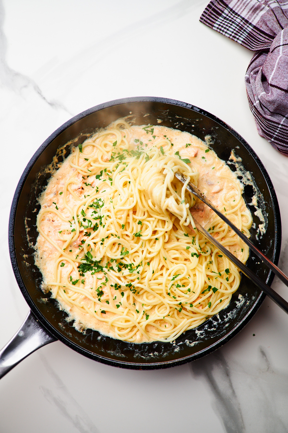 adding salmon back into the sauce for creamy garlic salmon pasta and then mixing in spaghetti with tongs