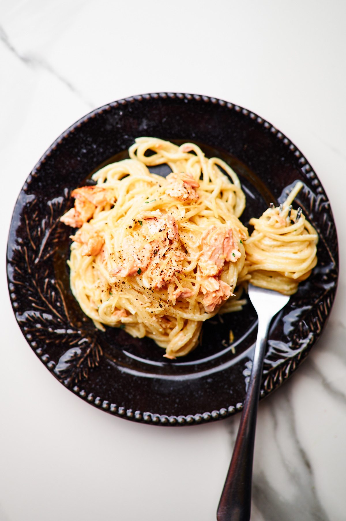 extreme close-up of serving tongs twirling creamy salmon spaghetti