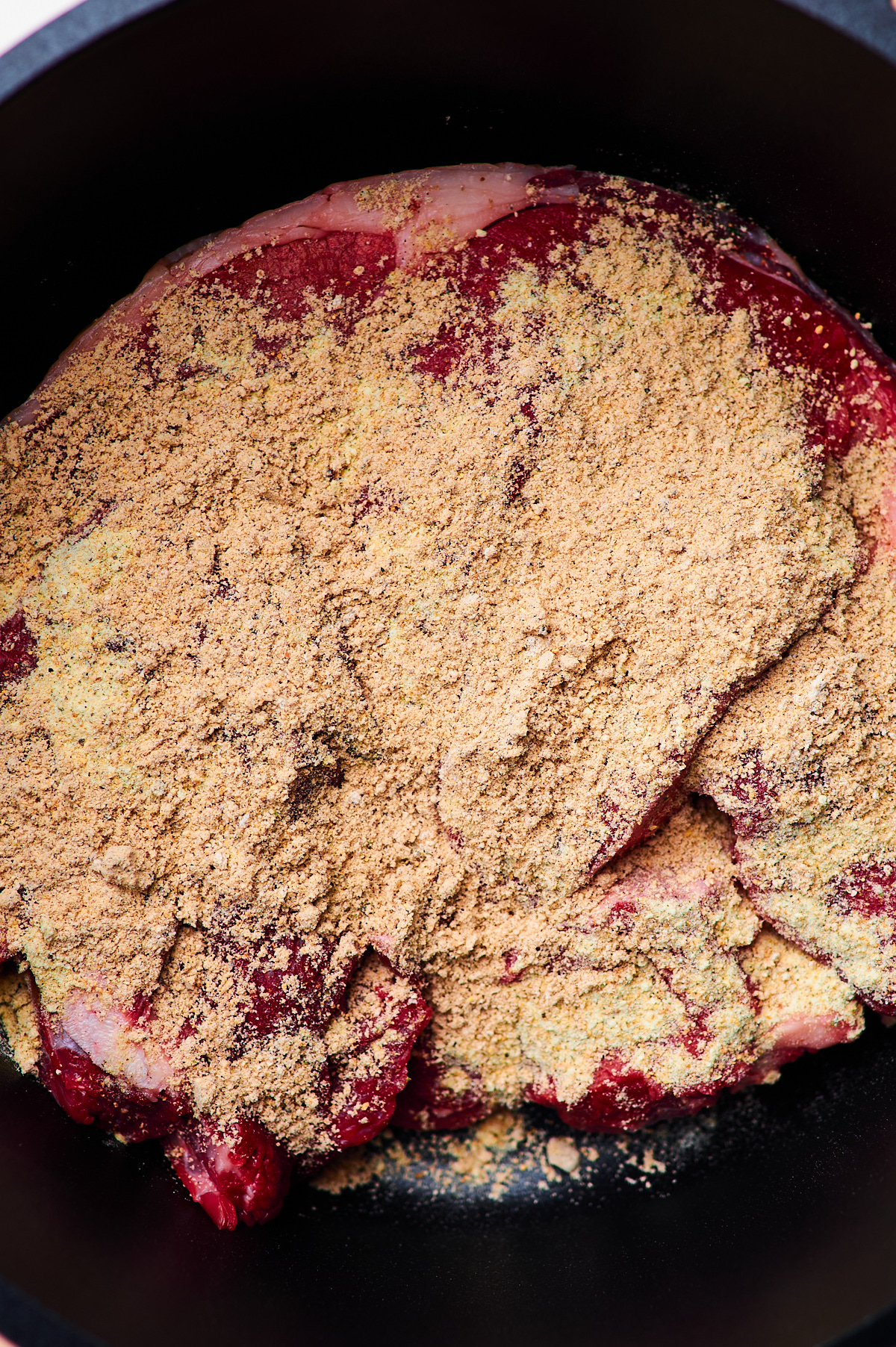 A close up of a chuck roast in a crockpot being sprinkled with seasoning